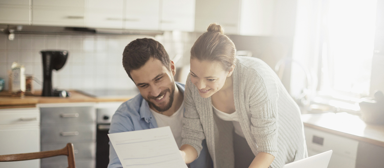 Pareja joven, sentados en su cocina, mirando una hoja y sonriendo Pareja joven, sentados en su cocina, mirando una hoja y sonriendo